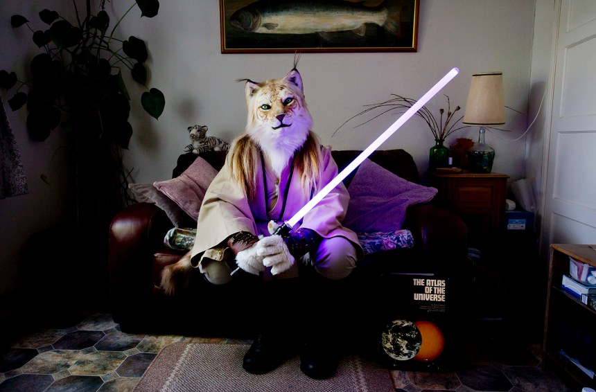 Fangorn, a Jedi tiger sits in his living room, Swansea From the series" At Home With The Furries" Throughout the year furries dress up in costume or fur-suit inspired by anthropomorphic characters from cartoons, comic strips, myths and videogames. The people inside the suits are by day computer programmers, engineers, mortgage brokers, lecturers even fursuit makers. Most furries have an affinity with animals but some also like to role-play or fursuit for fun. Over the course of a few years, I gained the trust of the furries in the UK and some of their members allowed me to visit them at home, these photographs were taken all over the country. Contact tom@tombroadbent.com for licensing rights